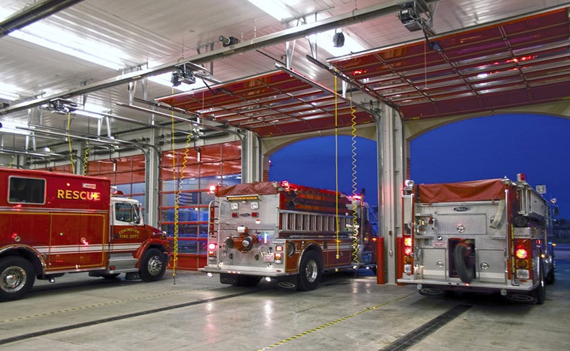 two fire trucks leaving the fire station while one is parked 